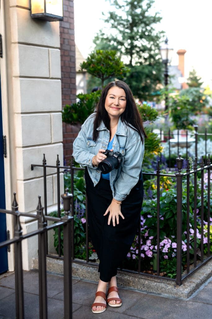 Your Orlando senior photographer standing by a rod-iron fence with her camera smiling softly in natural light.