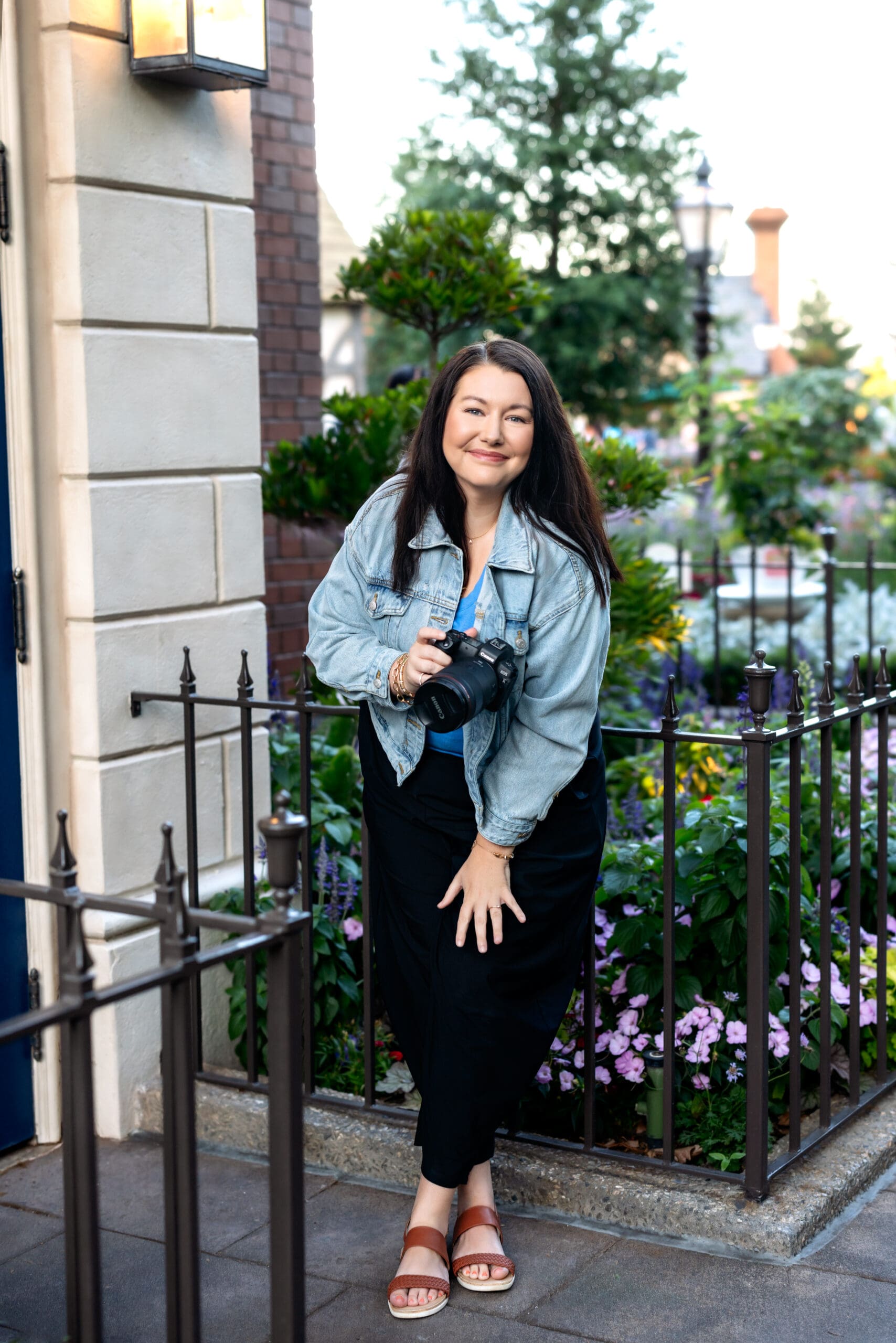 Ann, your Orlando senior photographer, sitting on fence with her camera, smiling softly in natural light.