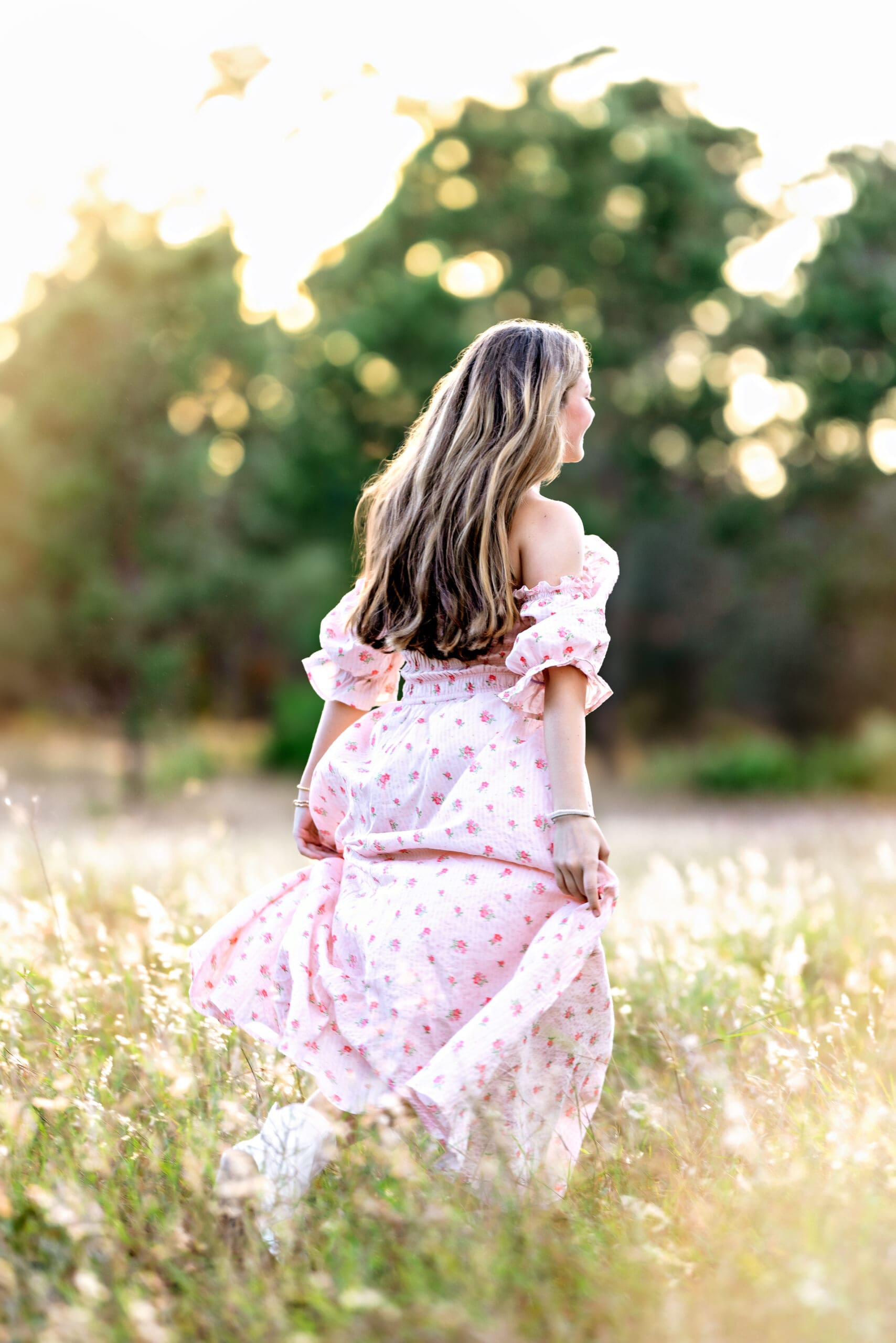High school senior running through a golden field at sunset in Winter Garden, Florida wearing a pink floral dress during her senior photo session.