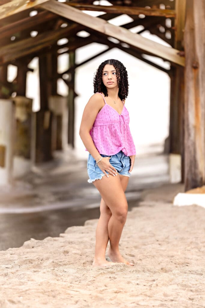 Senior photo of a girl posing with a vogue face and dramatic leading lines of a wooden pier behind her at Cocoa Beach.