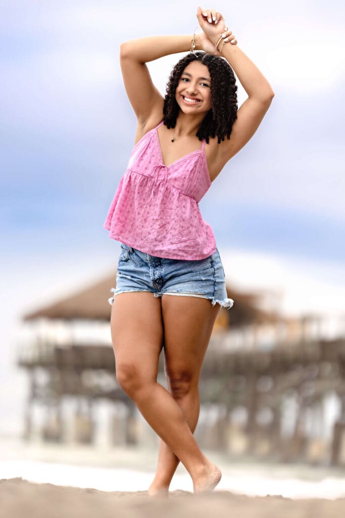 Senior girl posting confidently during a stormy beach session at Cocoa Beach wearing a pink tank top and cutoff jean shorts. 