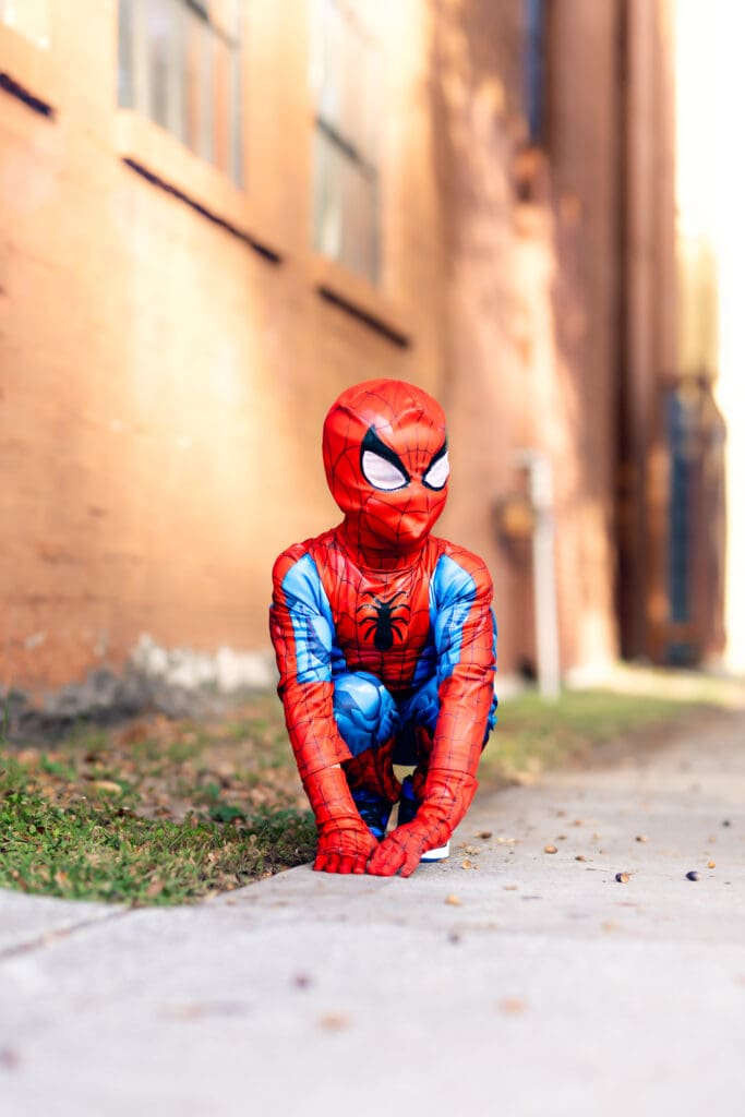 Kid in a Spider-Man-Costume sitting in his typical stance with a side profile visible as he looks off in the distance in Winter Garden.