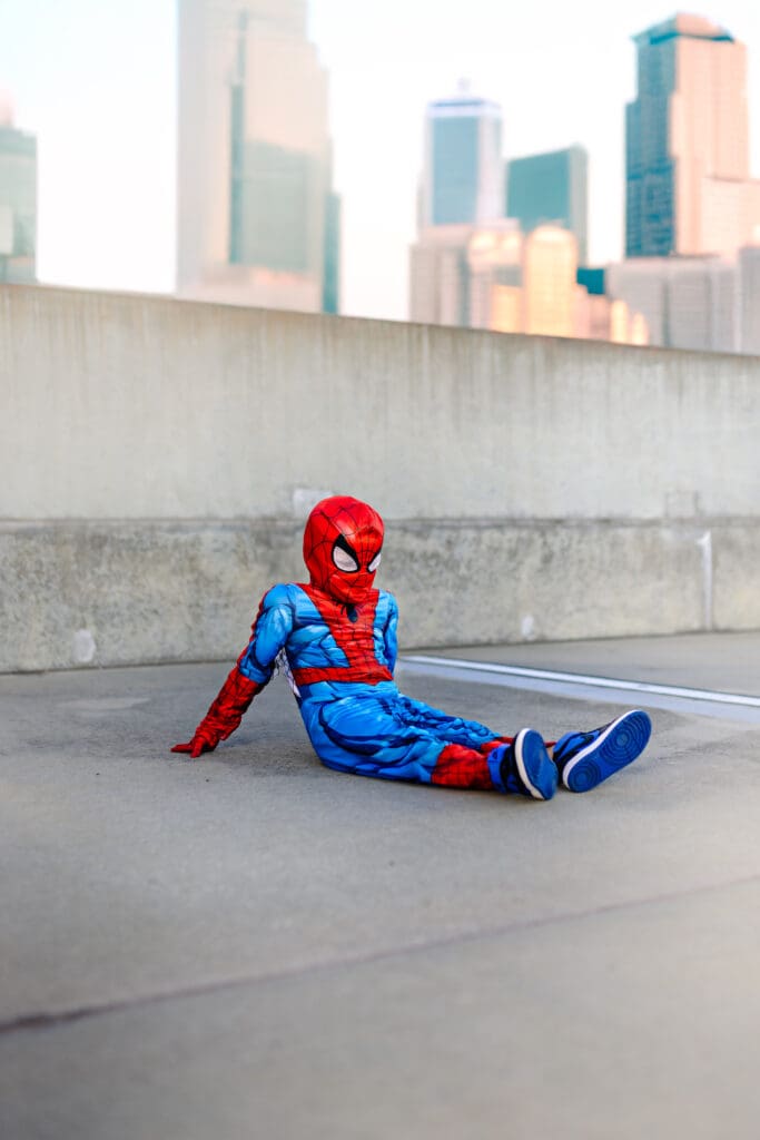 Boy in a Spider-Man costume sitting on a rooftop-style parking garage in Winter Garden, capturing the bold and imaginative spirit behind my senior photography sessions.