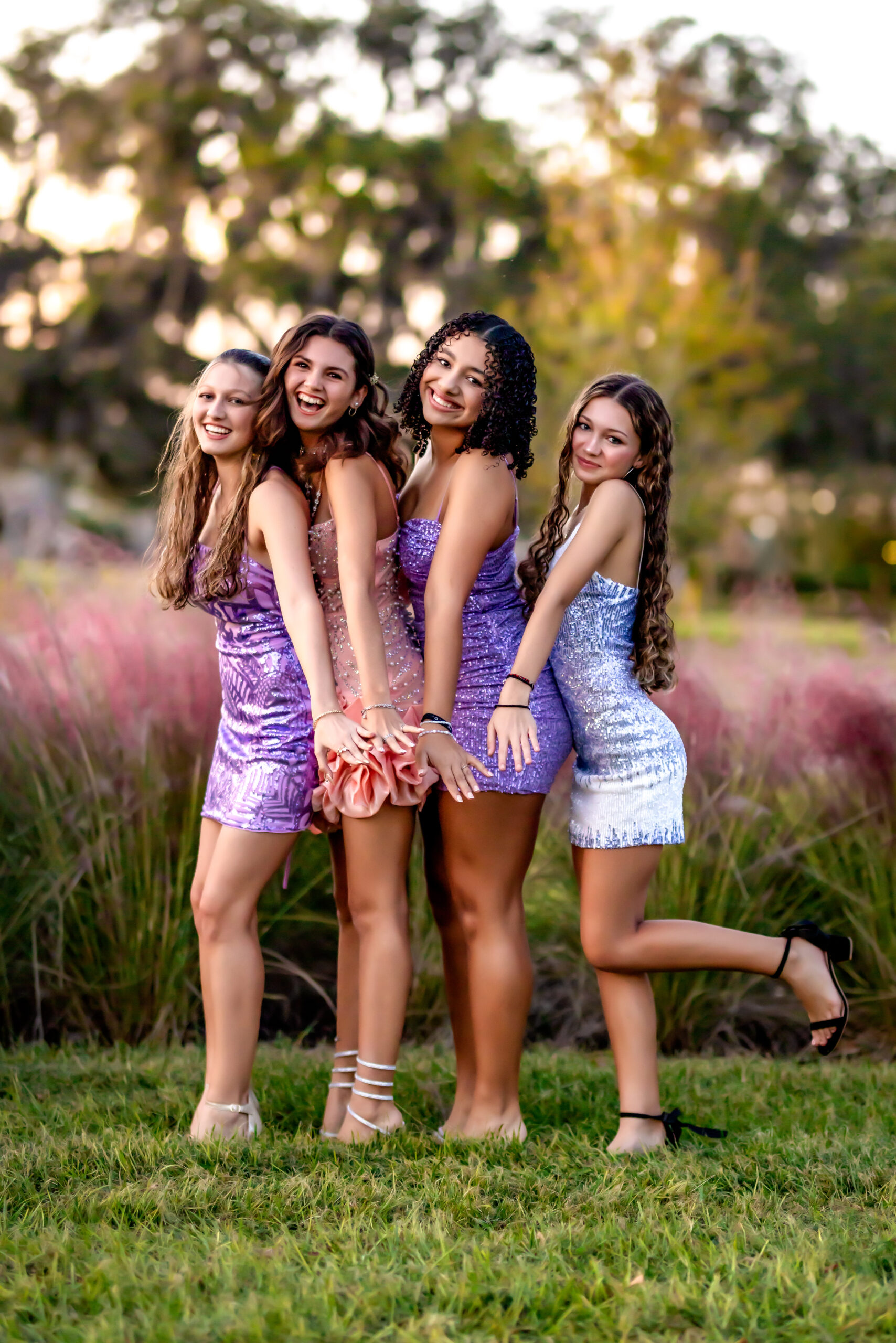 Four high school girls posing in sparkly homecoming dresses during golden hour in Winter Garden, Florida.