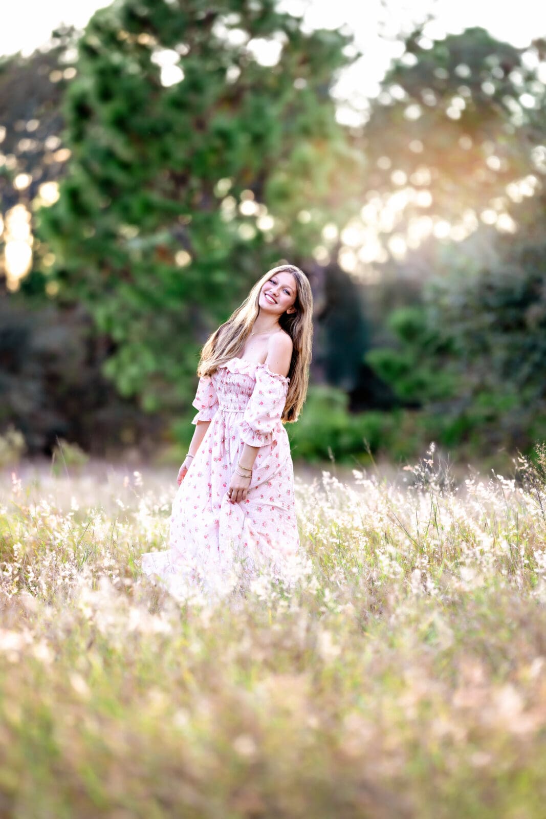 Senior girl twirling in a golden field during sunset in Winter Garden, Florida, wearing a soft pink floral dress.
