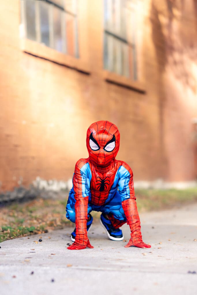 Young boy in a Spider-man costume crouched low with both hands on the sidewalk posing against a brick wall in Winter Garden during an epic hero inspired shoot.