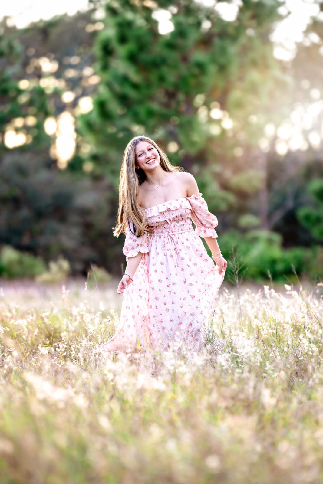 High school senior walking through tall grass at golden hour, smiling and wearing a long floral dress in Winter Garden, Florida