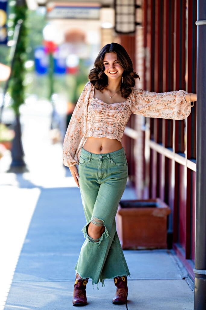Senior girl in green pants walking with confidence outside a stylish building in Downtown Winter Garden.