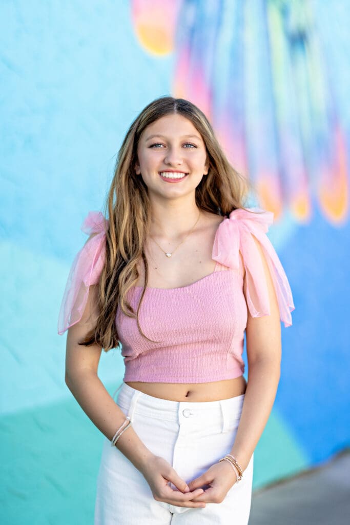 Senior girl in pink top with puffy sleeves standing against a blue pastel wall mural in Downtown Winter Garden.