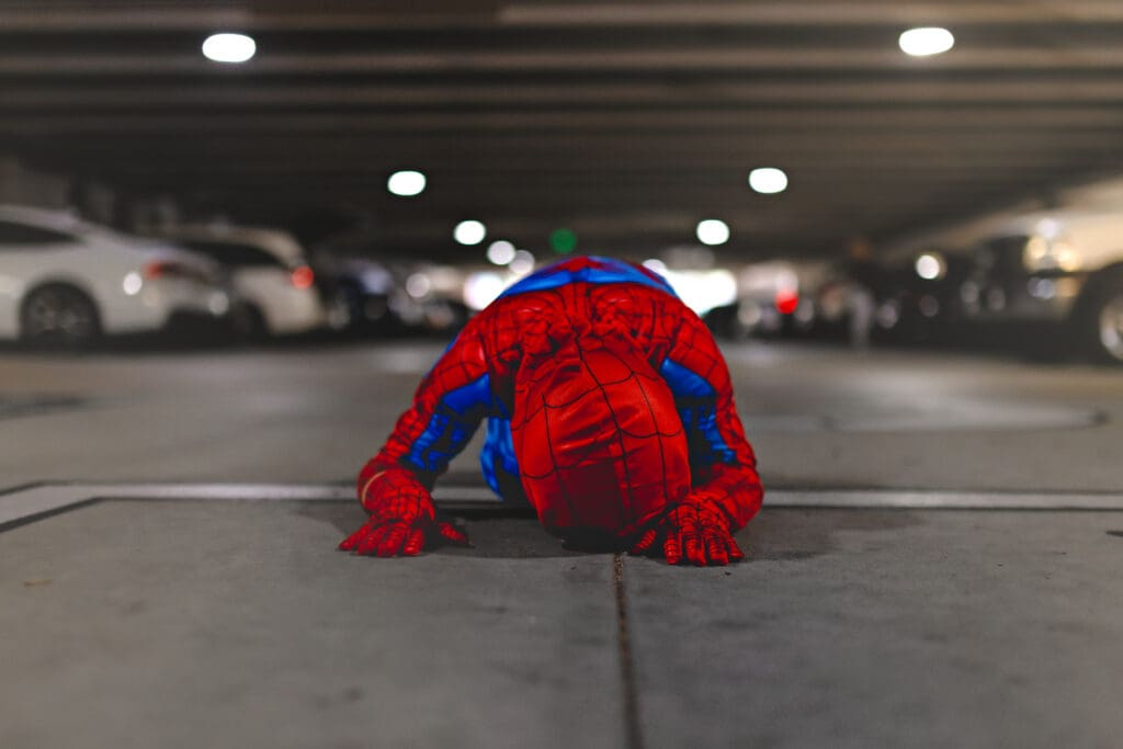 Young boy in a Spider-Man costume lying face down on the concrete in a parking garage in Winter Garden, showing the playful, personality-driven style behind senior photography sessions with Petal and Stone Photography.