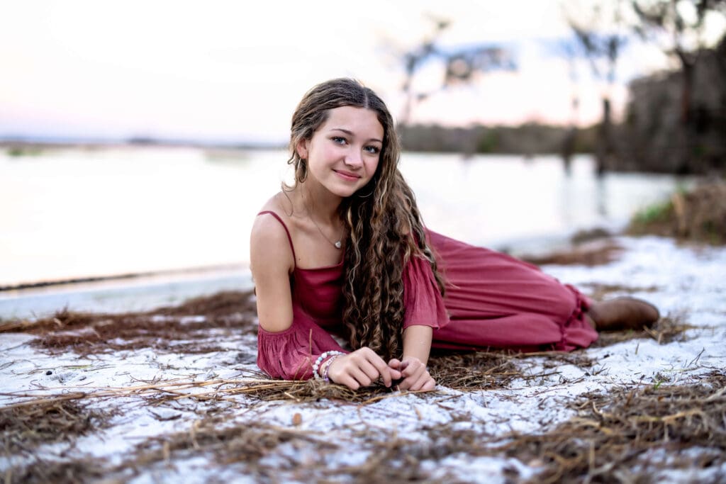 Lake Louisa State Park senior photo of a girl in a burgundy dress lying near the water with soft blue hour light, giving cottagecore vibes and watercolor-worthy beauty.

