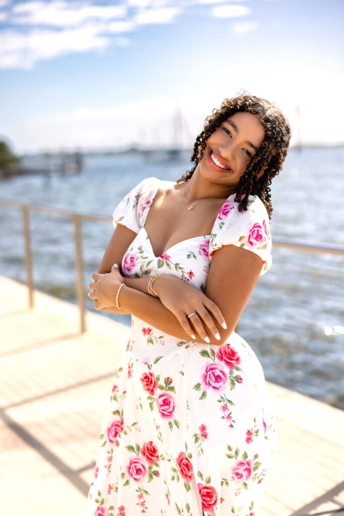 High school senior posing by the water in a white floral dress during her Cocoa Beach senior photo session near Orlando, Florida.