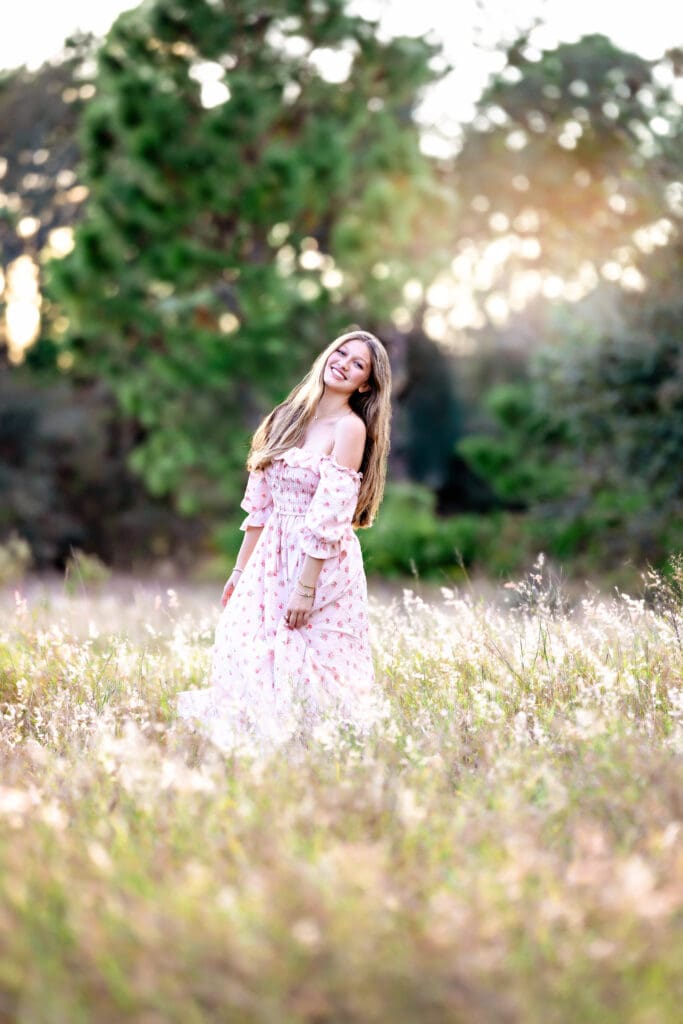 Beautiful senior girl twirling in Winter Garden Florida at sunset in long floral pink dress.