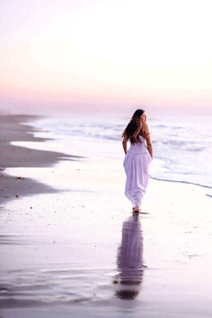 High school senior girl walking along the shoreline at sunrise during a luxury senior photo session in Central Florida at Cocoa Beach photographed by Petal and Stone Photography.