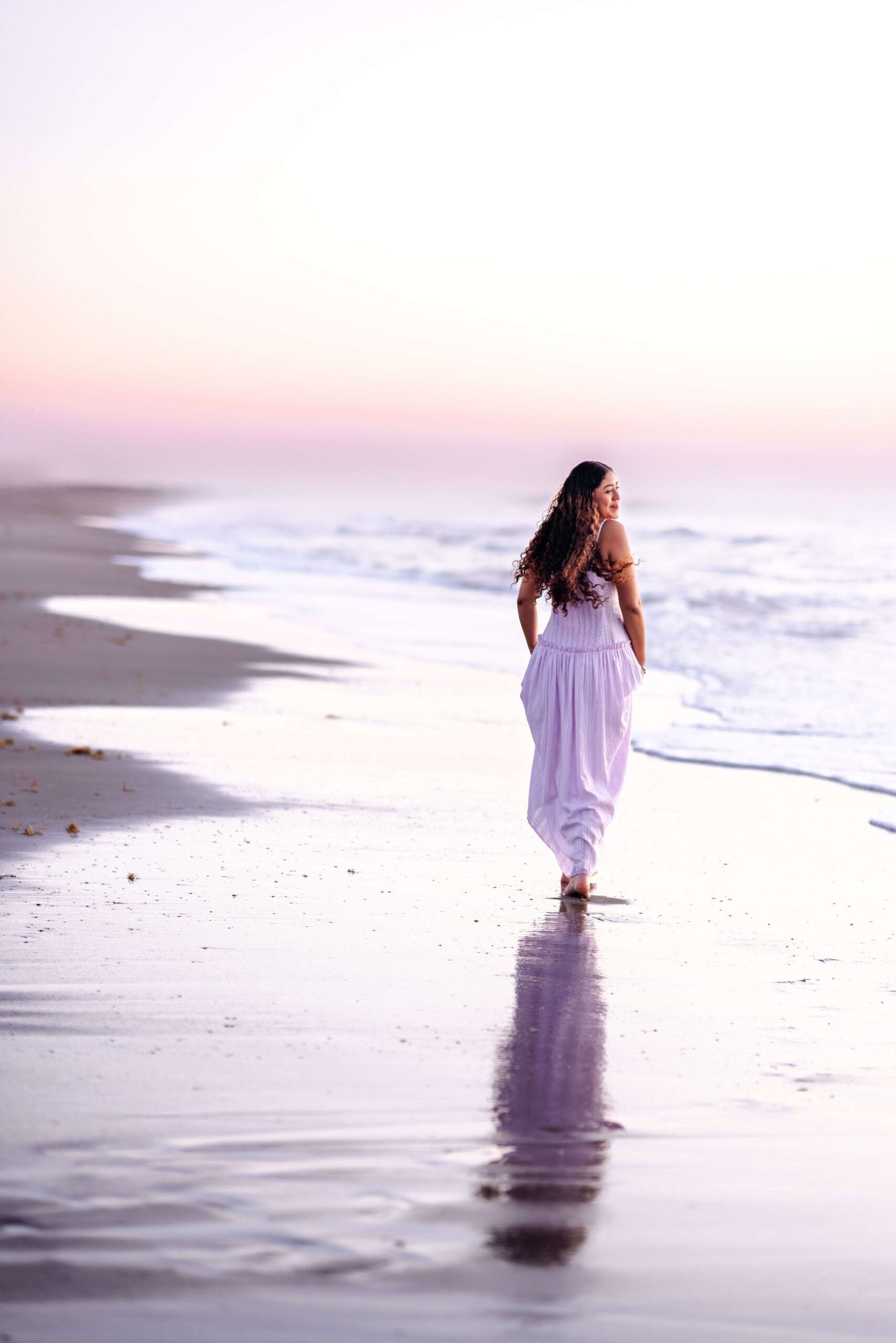 High school senior girl walking along the shoreline at sunrise during a luxury senior photos session in Central Florida photographed by Petal and Stone Photography.